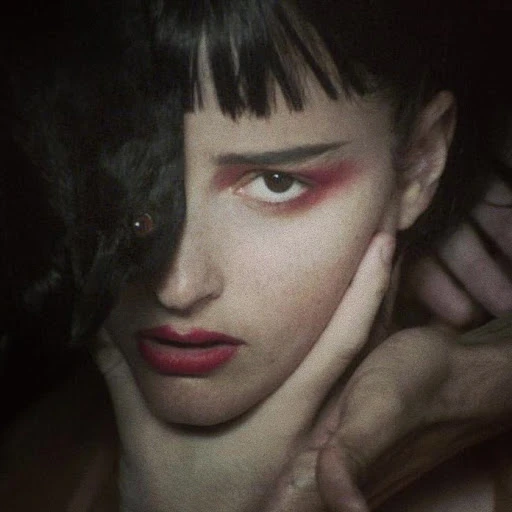 Portrait of a woman with red eye makeup and lipstick, holding her face with a hand, showcasing beauty and makeup in a studio setting.