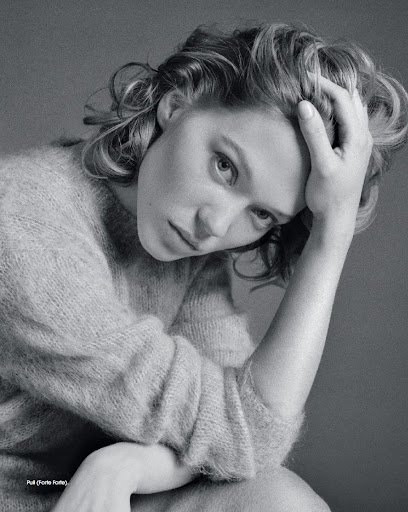 Black and white portrait of a woman with her hand on her head, wearing a soft textured sweater, gazing at the camera.