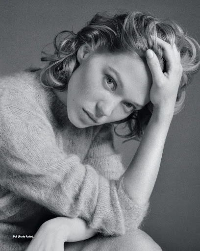 Black and white portrait of a woman with her hand on her head, wearing a soft textured sweater, gazing at the camera.