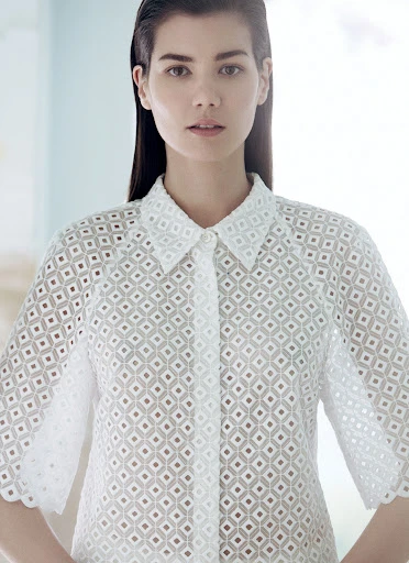 Close-up studio shot of a young adult woman with fair skin and dark hair wearing a white eyelet shirt with a collared neckline.