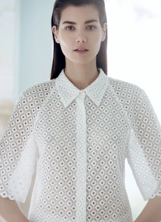 Close-up studio shot of a young adult woman with fair skin and dark hair wearing a white eyelet shirt with a collared neckline.