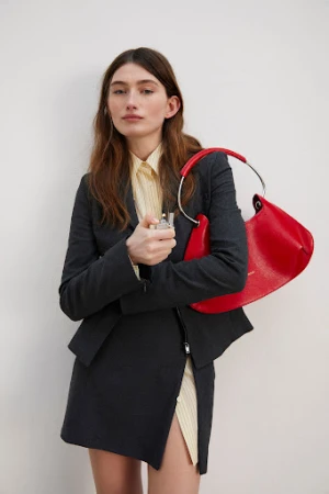 Model in dark grey suit jacket and skirt holding a bright red handbag against plain white wall