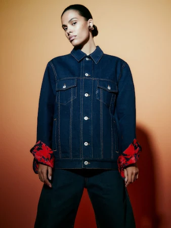 Model in dark blue denim jacket with red floral cuffs against a warm gradient background