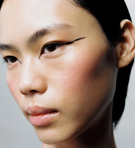Close-up portrait of an Asian woman with fair skin and black eyeliner, showcasing beauty and makeup in a studio environment with soft lighting.