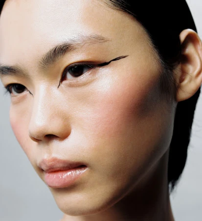 Close-up portrait of an Asian woman with fair skin and black eyeliner, showcasing beauty and makeup in a studio environment with soft lighting.
