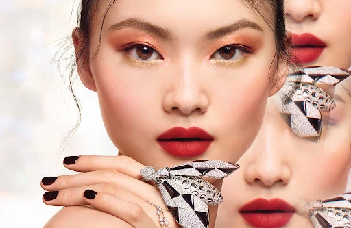 Portrait of a young Asian woman showcasing makeup with orange and red eyeshadow, red lipstick, and large diamond and black rings.