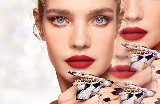 Close-up beauty portrait of a woman with red lipstick, golden eye makeup, and a bejeweled insect ring by Nolwenn Quintin.