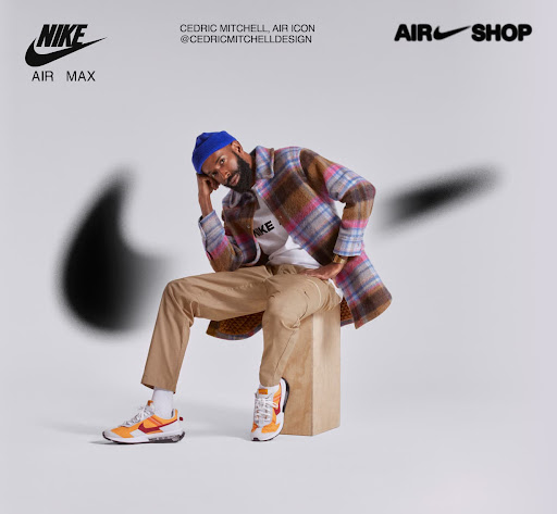 A man wearing a colorful plaid jacket and a blue beanie is seated on a wooden block wearing Nike sneakers in a studio shot.