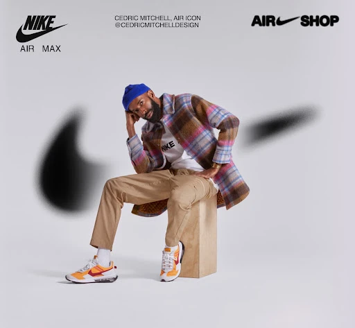 A man wearing a colorful plaid jacket and a blue beanie is seated on a wooden block wearing Nike sneakers in a studio shot.
