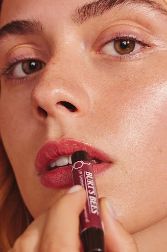 Close-up shot of an adult female applying deep red lipstick from Burt's Bees. The camera focuses on the model's face and hands.