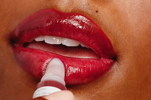 Macro shot of a woman's face shows an application of glossy red lip stain, highlighting her full lips and smooth skin.