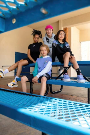 Four young people in Puma branded clothing and shoes sit on a blue metal bench outside, showcasing a mix of modern streetwear fashion.