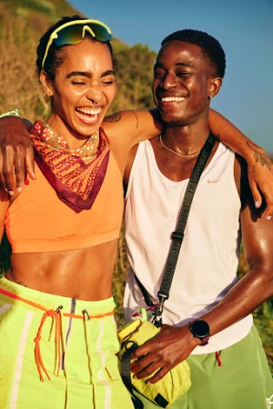 Smiling black woman and black man standing outdoors with arms around each other in athletic wear.