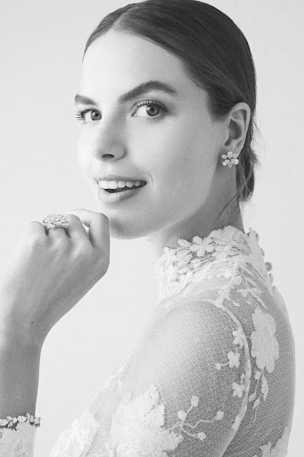 Close-up in black and white of a woman in an elegant lace dress with jewelry, gazing over her shoulder with a slight smile.