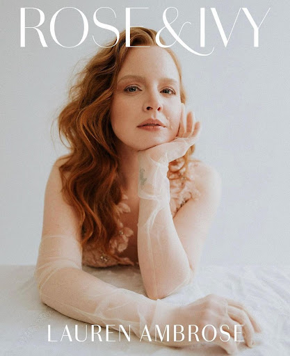 Portrait of red-haired actress Lauren Ambrose wearing sheer gloves and posing in front of a bright white studio backdrop.