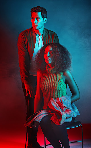 Stylish shot of a man and woman in a studio with red and blue lighting. The woman sits on a stool, and the man stands behind her.