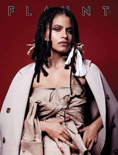 Zazie Beetz poses for a fashion magazine cover with a red background, wearing a beige jacket and strapless top with braided hair.