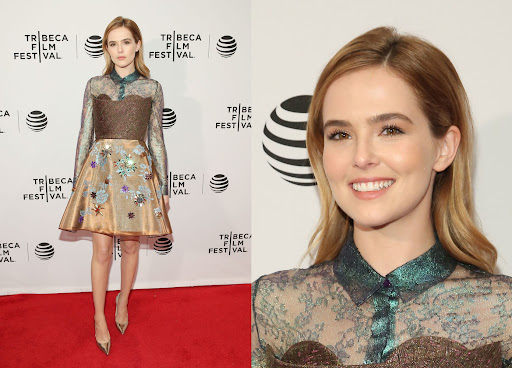 Zoey Deutch wearing a patterned metallic dress on a red carpet with Tribeca Film Festival backdrop branding.