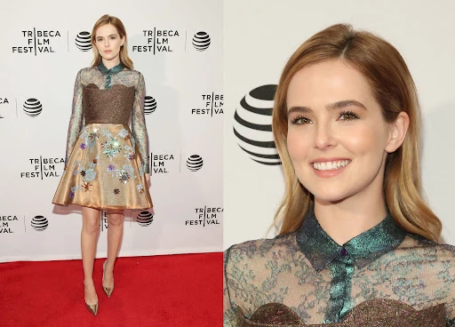 Zoey Deutch wearing a patterned metallic dress on a red carpet with Tribeca Film Festival backdrop branding.