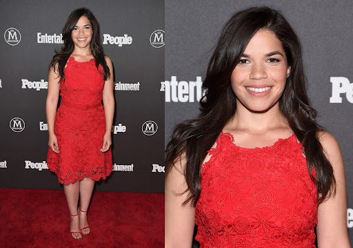 America Ferrera poses on a red carpet in a red, knee-length, sleeveless lace dress and strappy red high-heeled shoes, smiling warmly.