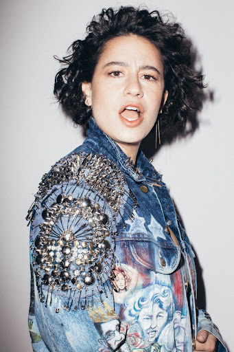 Young woman in embellished denim jacket posing indoors against a neutral backdrop, portrait shot, eye-level view, studio lighting.