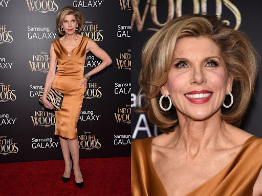 Christine Baranski poses on the red carpet in a gold dress and black heels in front of a movie advertisement backdrop.