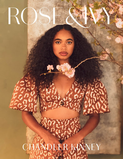 Fashion editorial shot of Chandler Kinney wearing a patterned two-piece outfit, posing in front of a textured wall with flowering branches.