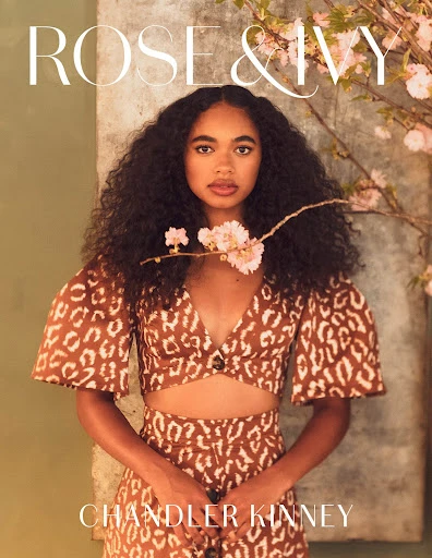 Fashion editorial shot of Chandler Kinney wearing a patterned two-piece outfit, posing in front of a textured wall with flowering branches.