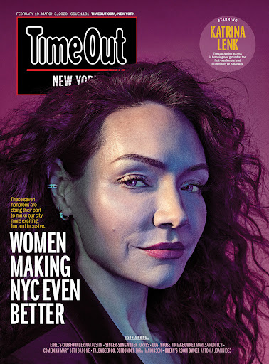 Close-up magazine cover portrait of Katrina Lenk with dark curly hair and subtle makeup against a purple background.