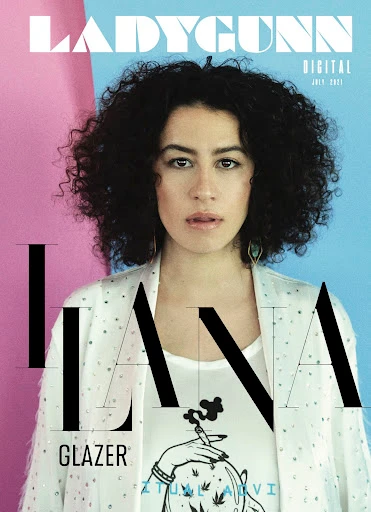 Portrait of a woman with dark curly hair wearing a white patterned jacket against a pink and blue background