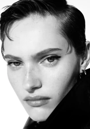 Close-up monochrome portrait of a model with short dark hair and winged eyeliner against a white background.