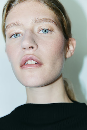 Close-up portrait of a young adult woman with blue eyes and fair skin, wearing a black top against a light background.