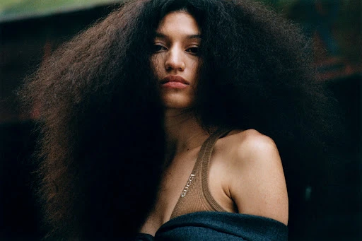 Close-up portrait of a woman with voluminous dark hair wearing a ribbed brown top and dark jacket in Paris.