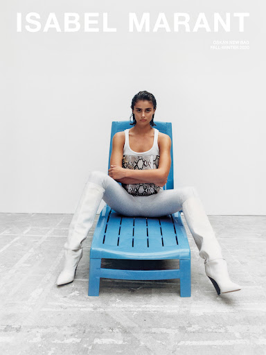 Fashion ad featuring a model in a tank top and boots, seated on a blue lounge chair against a bright white backdrop in a studio setting.