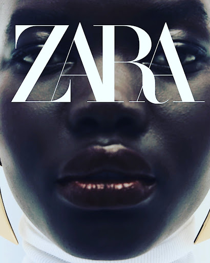 Close-up portrait of a model with dark skin and glossy lips wearing a white turtleneck and gold earrings, styled by Sohphea.