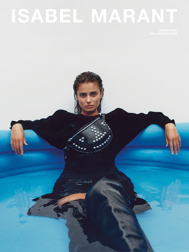 Fashion editorial shot of Taylor Hill modeling Isabel Marant in a blue water pool, wearing a studded fanny pack and a dark outfit.