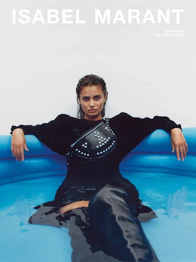 Fashion editorial shot of Taylor Hill modeling Isabel Marant in a blue water pool, wearing a studded fanny pack and a dark outfit.