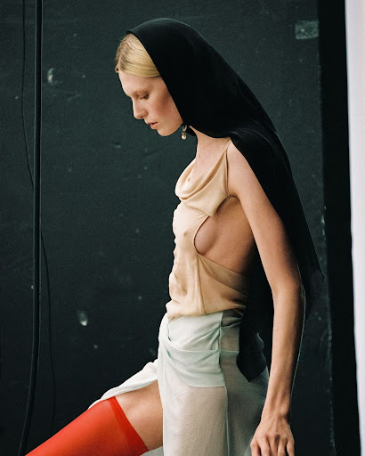 Fashion photography of a woman in a headscarf, a light-colored top, and red stockings against a dark studio backdrop. 