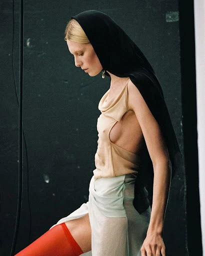 Fashion photography of a woman in a headscarf, a light-colored top, and red stockings against a dark studio backdrop. 
