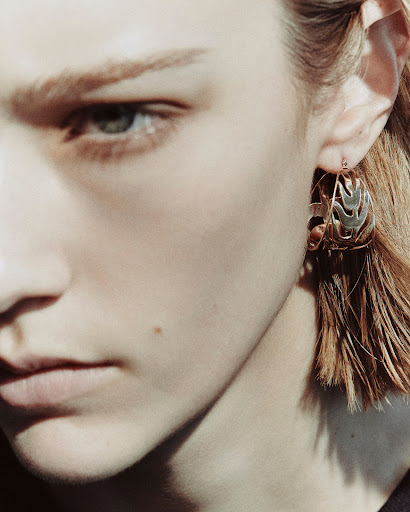 Close-up portrait of a model wearing an intricate metallic hoop earring with makeup by Sohphea in Paris
