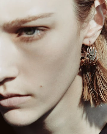 Close-up portrait of a model wearing an intricate metallic hoop earring with makeup by Sohphea in Paris
