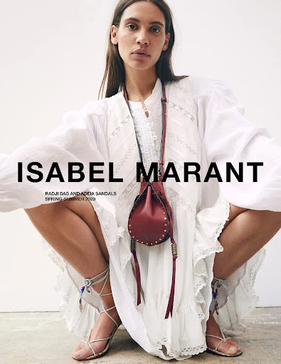 Fashion shot featuring an adult female model posing in a white dress and leather bag, showcasing Isabel Marant clothing and accessories.