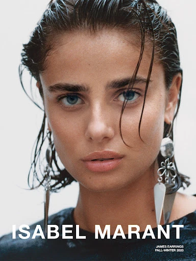 Close-up studio shot of a woman with wet hair wearing large silver earrings and a dark top, against a neutral background.