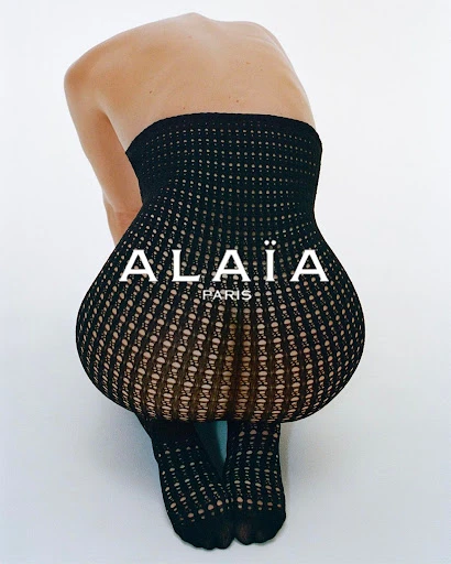 Woman wearing patterned black hosiery crouching in a white studio. Fashion-forward hosiery for women. Designer stockings and tights.