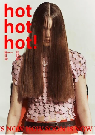 Model with long brown hair covering face wearing a pink disc-embellished top and red bottoms against a plain background