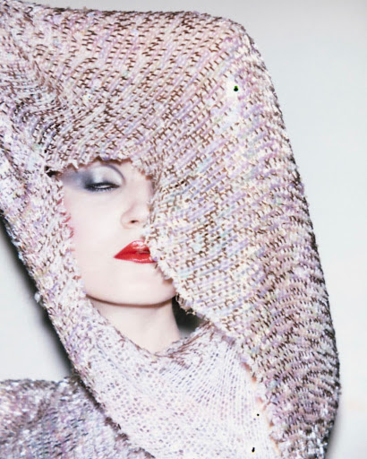 Close-up studio shot of a glamorous woman wearing a glittering lavender gown and dramatic makeup, with fabric draped over her head.