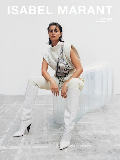 Model wearing white knit sweater, white trousers, and tall boots seated on a transparent inflatable object
