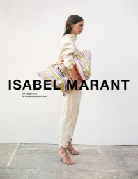 Model standing sideways holding a striped canvas tote bag wearing a cream utility jumpsuit against a plain wall.