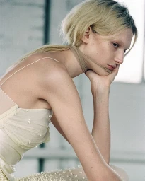 Close-up portrait of a blonde model wearing a pale strappy dress with her chin resting on her hand in Paris