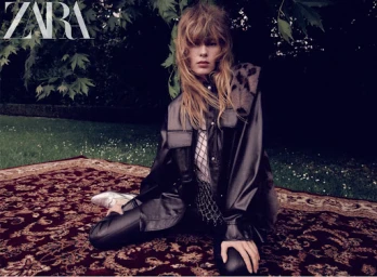 Model with long fringe wearing a black leather shirt and trousers kneeling on a patterned rug outdoors on grass